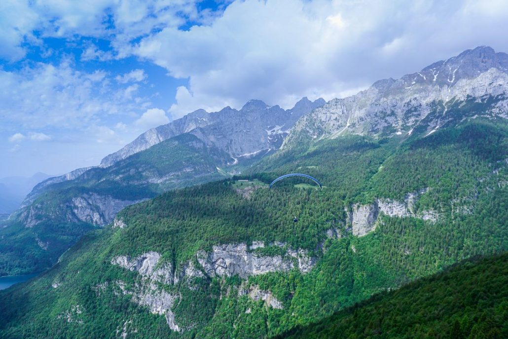 Glorious views of a paraglider flying above Lake Molveno with the Brenta Dolomites behind them