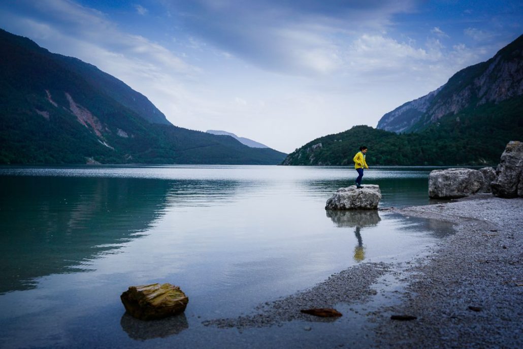 Girl in a yellow coat jumping off a rock on Lake Moreno in Trentino Italy