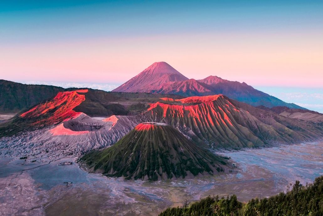 The spectacular Mount Bromo in Indonesia at sunrise covered in pinks, reds and orange colours from the sun