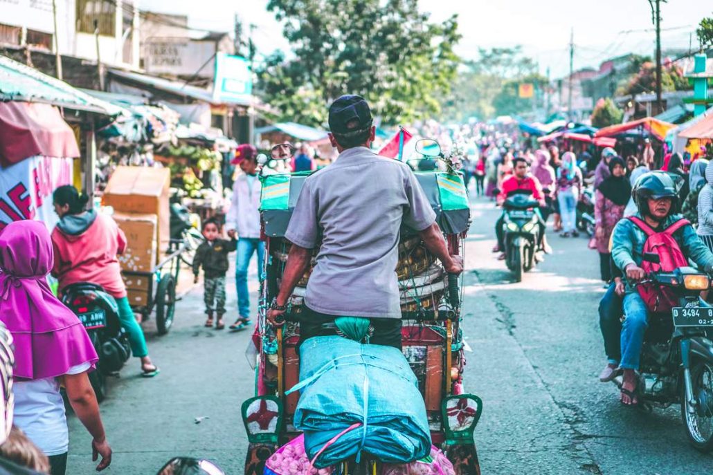 Trader cycling through the streets of Bandung in a market with fruit and vegetables