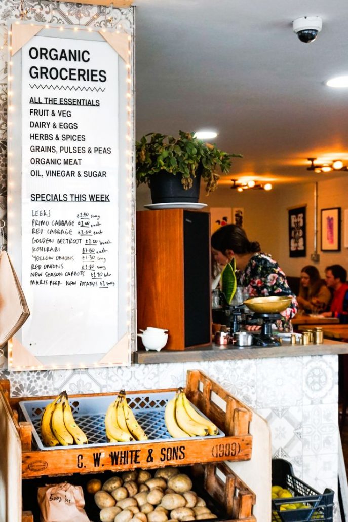 A lady choosing her dish within Eat Your Greens with a clean and white menu on the wall showing her what she can choose