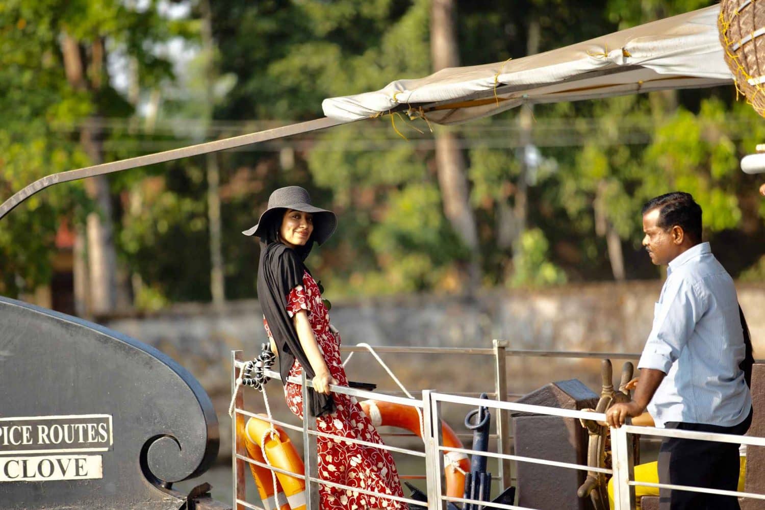 Woman looks at camera while on houseboat. Man opposite woman looks at river.