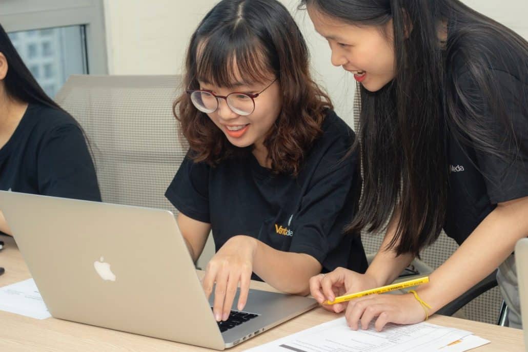 Two girls, one wearing glasses and one without, looking at a Macbook.