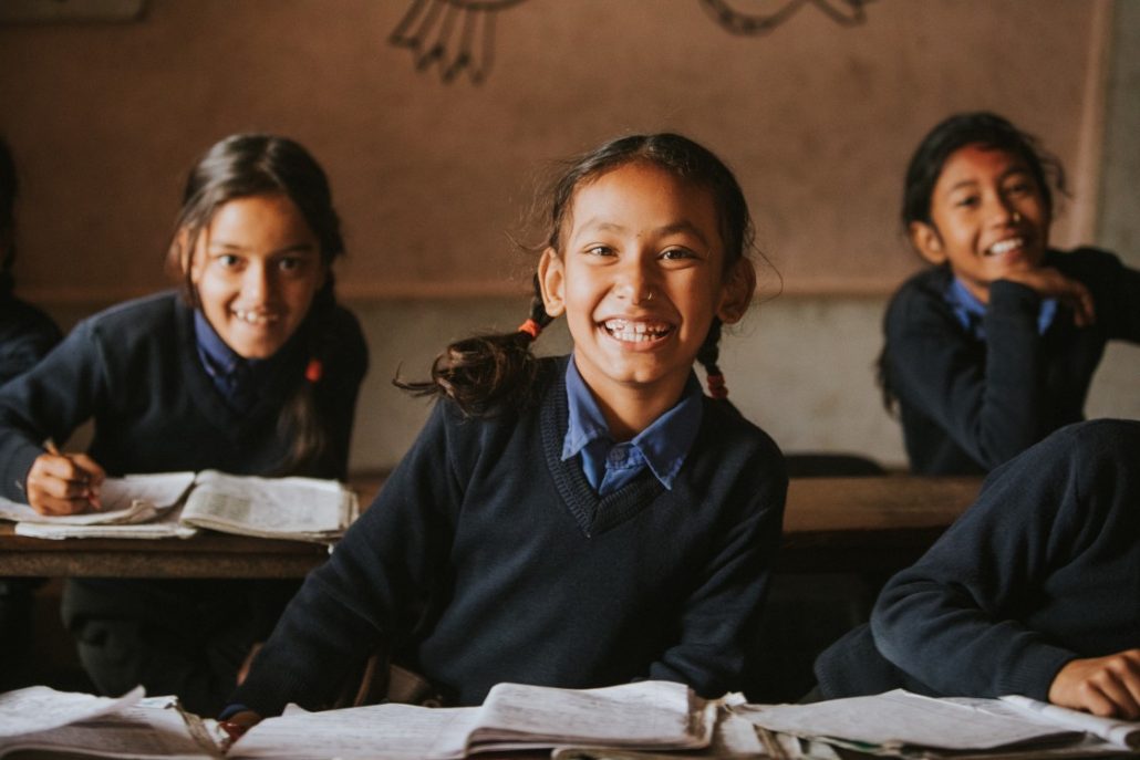 A group of young students in uniforms sitting and smiling in a class room