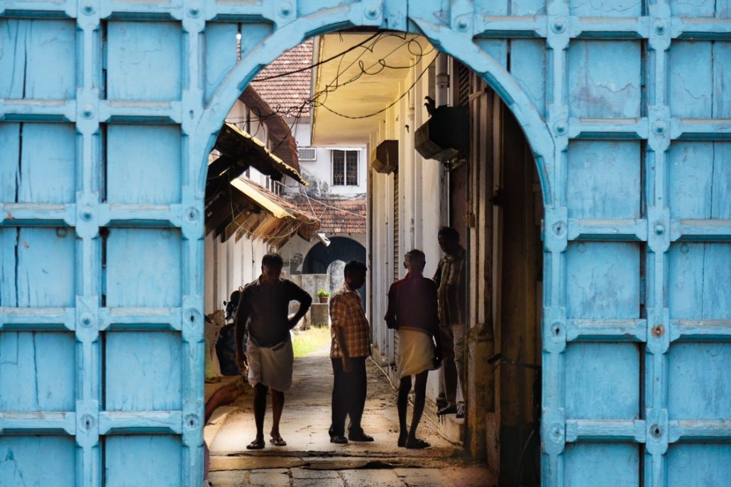 Four local men standing in an alleyway, framed by an archway that have been cut out of a blue wall.