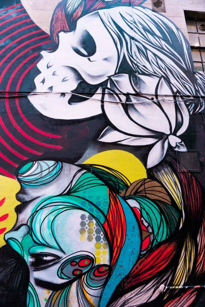 A woman looking at the reflection of her skull on a wall street art piece in Brighton