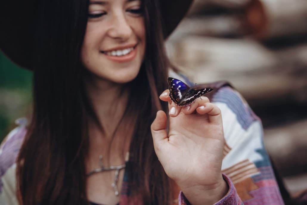 Happy stylish traveler girl in hat holding beautiful colorful butterfly on hand